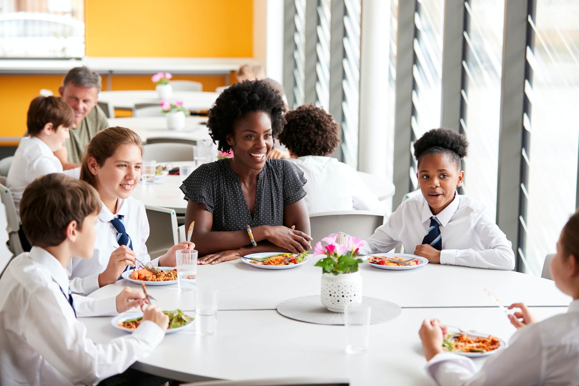 Female Teacher With Group Of High School Students In Cafeteria