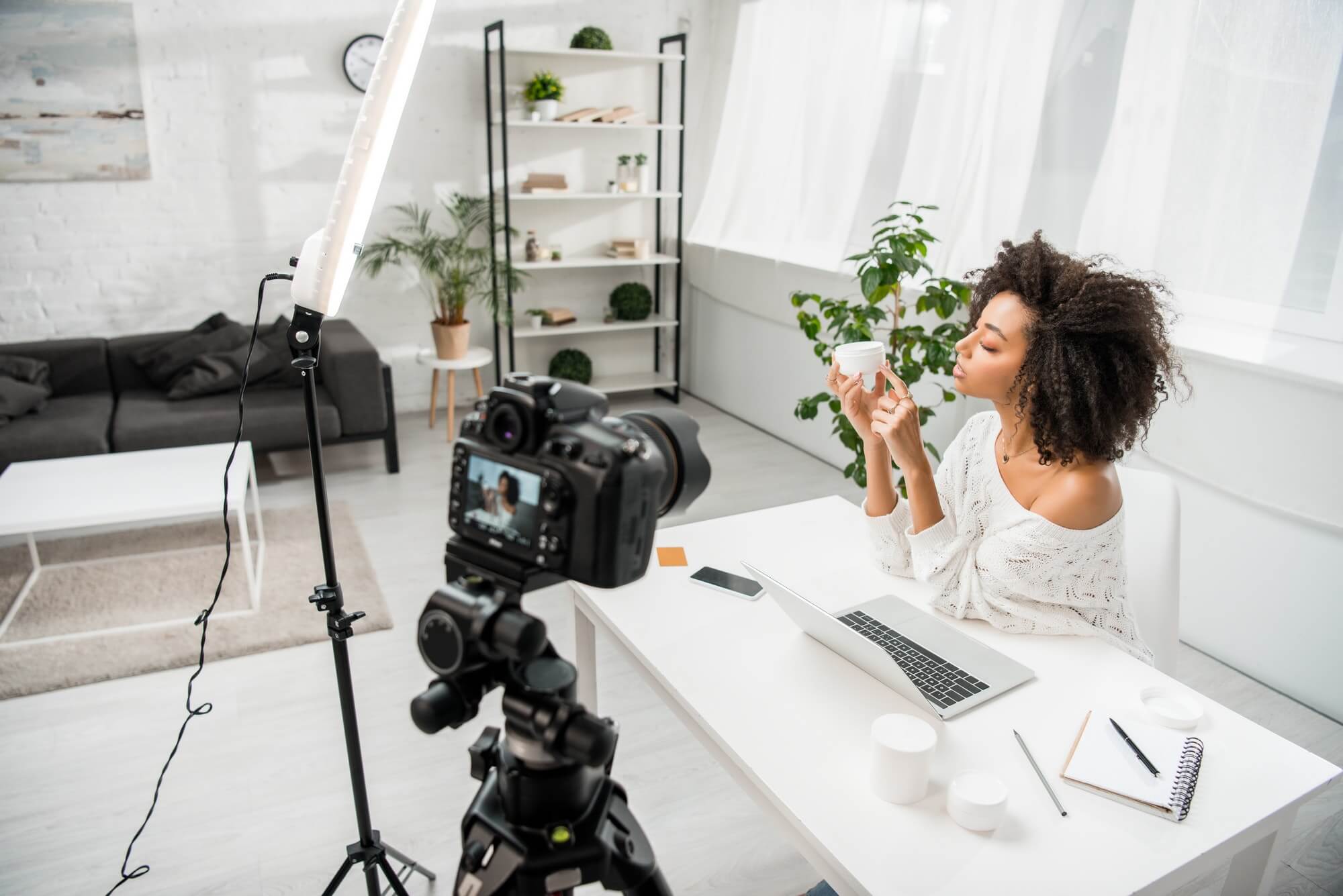 selective focus of african american influencer holding container with cosmetic cream near digital