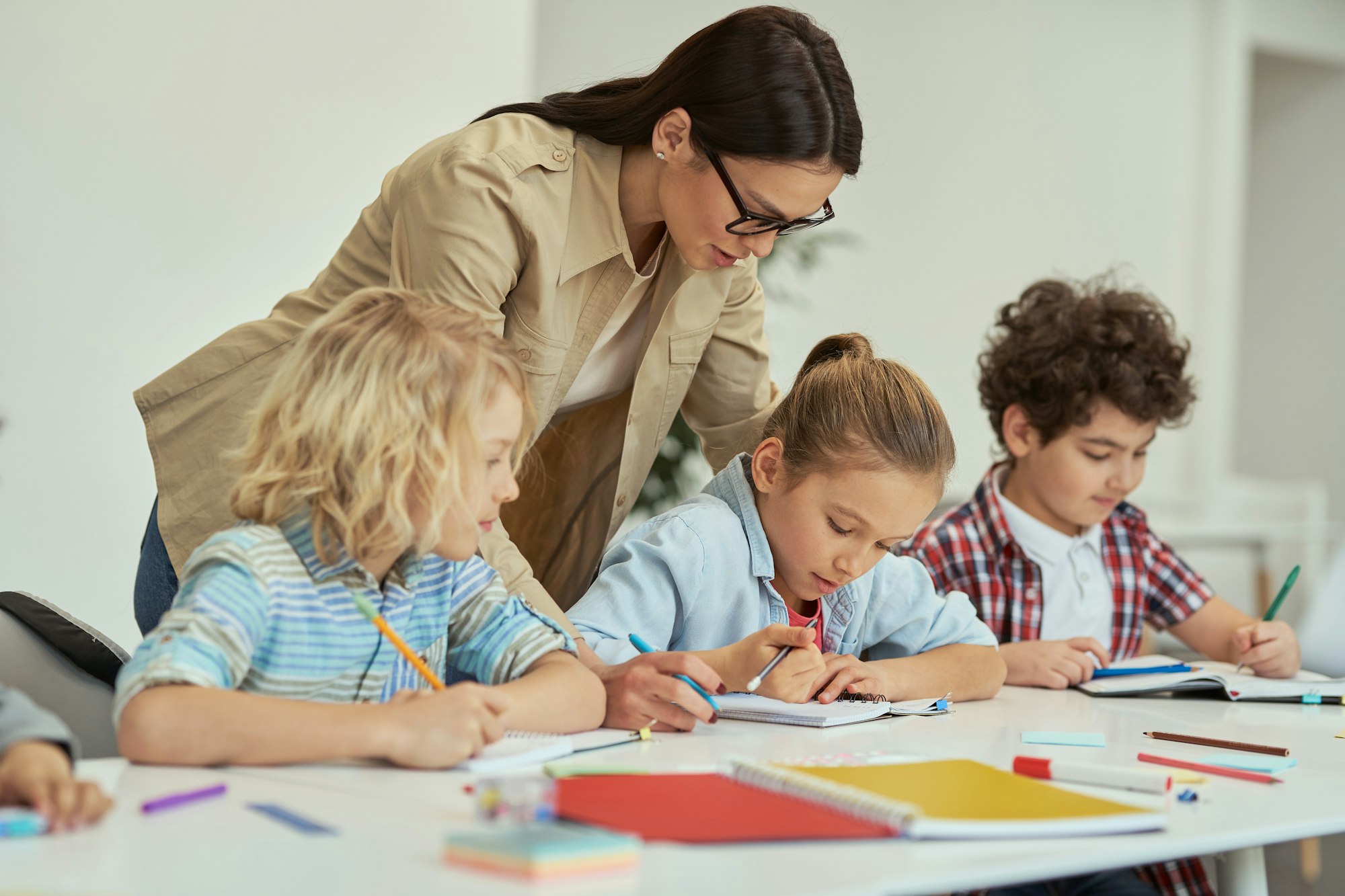 Excellence. Kind young female teacher in glasses helping her little schoolchildren in a classroom