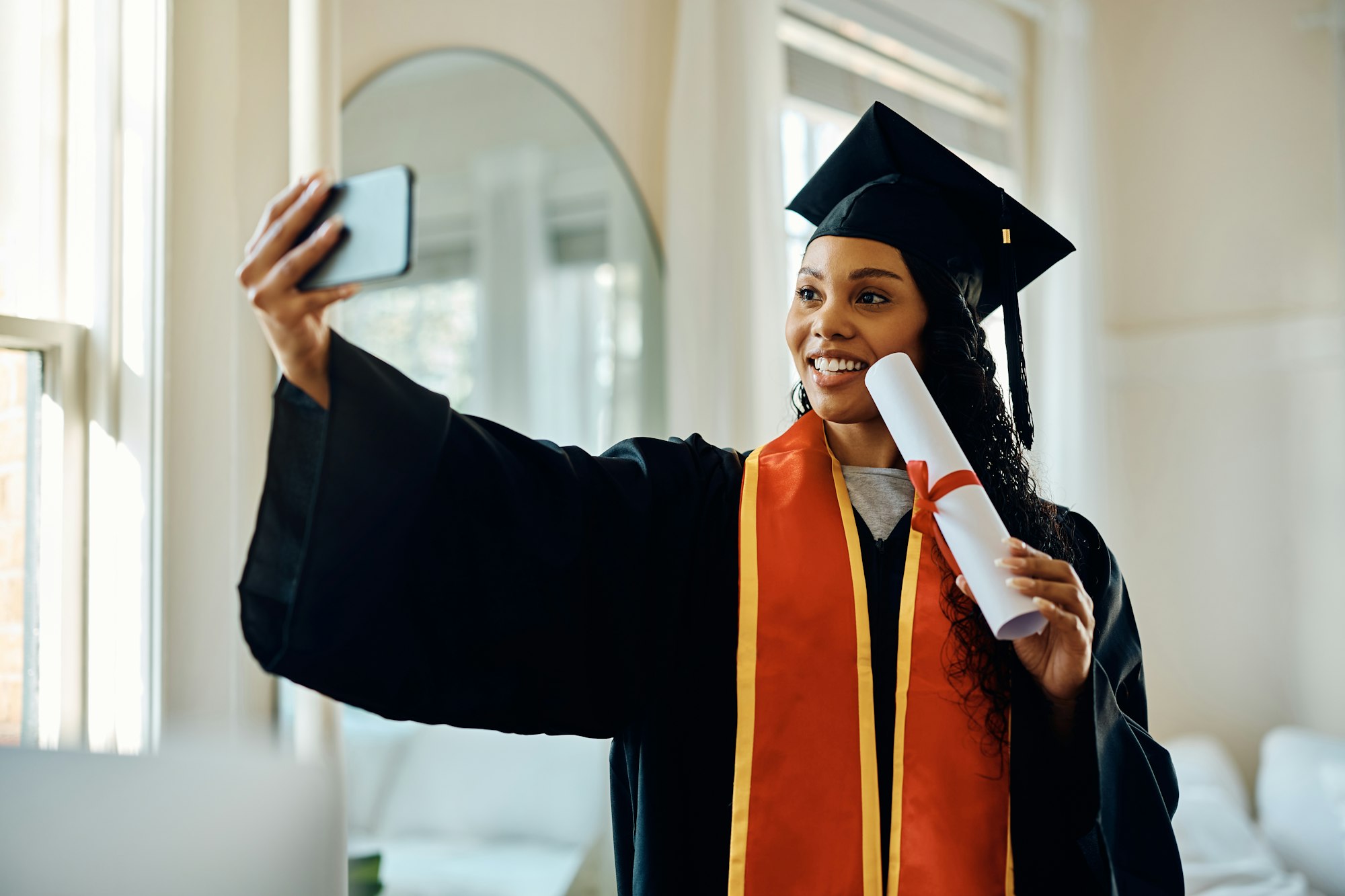 Happy African American graduate taking selfie after receiving university certificate.