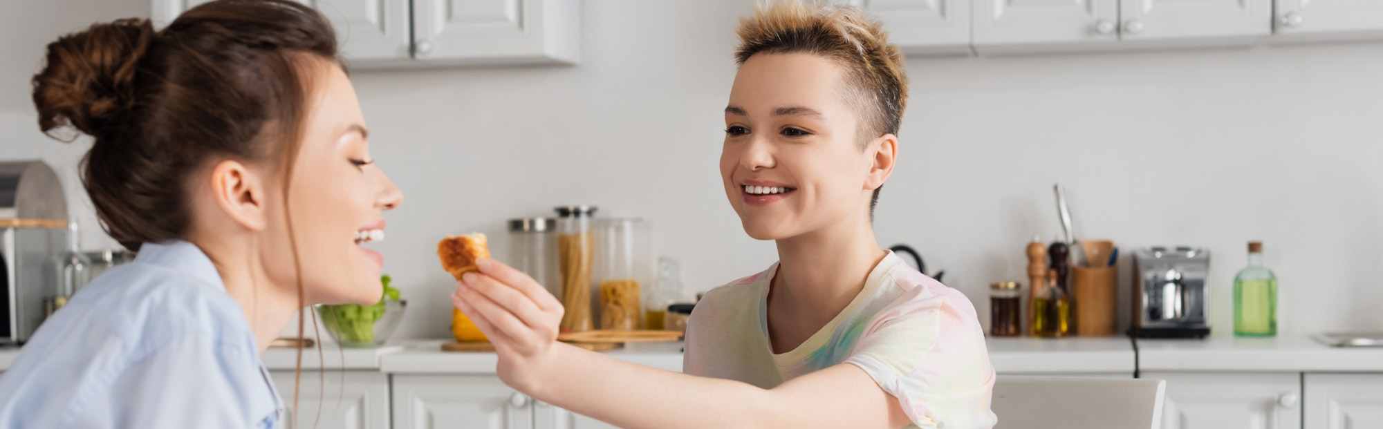 happy pangender person feeding partner with delicious croissant, banner