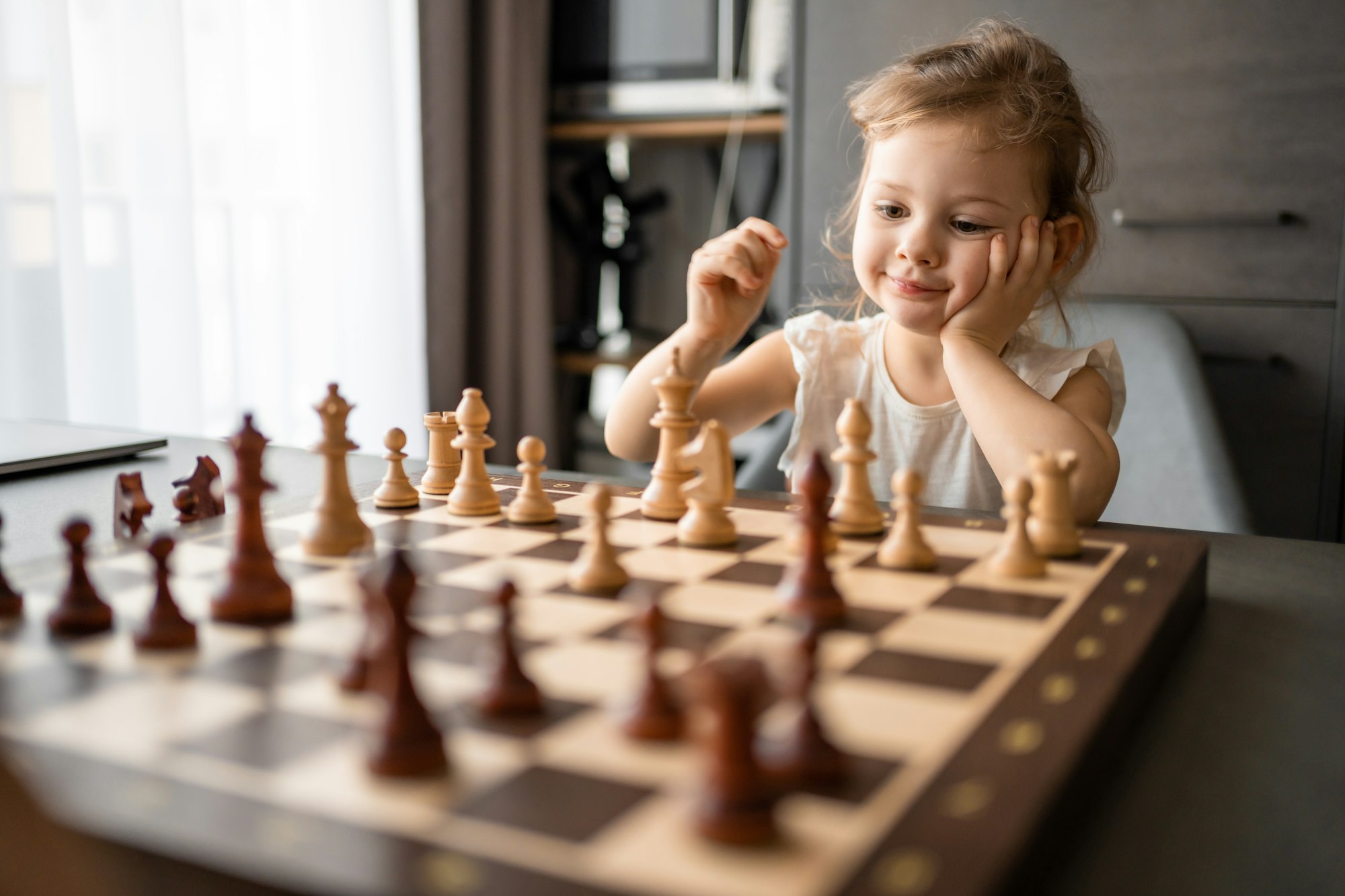 Little girl playing chess at the table in home kitchen. The concept early childhood development and