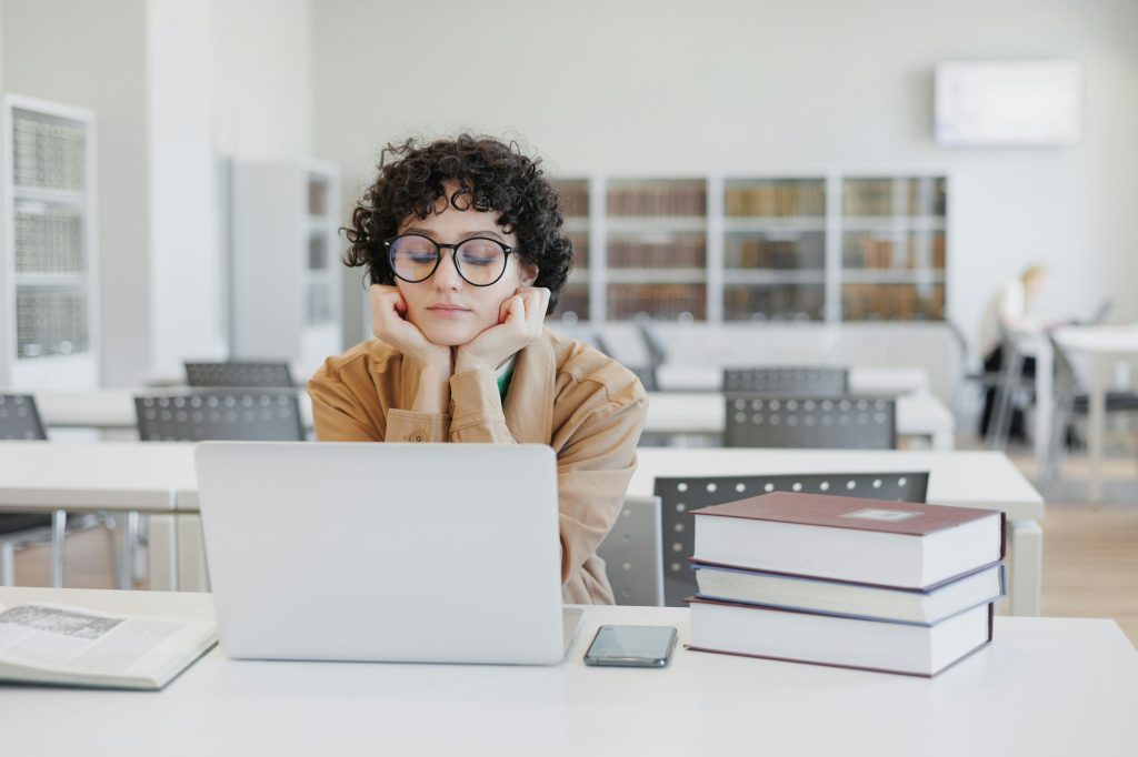 thoughtful woman works in library, watches an educational webinar on Internet, is bored. coworking