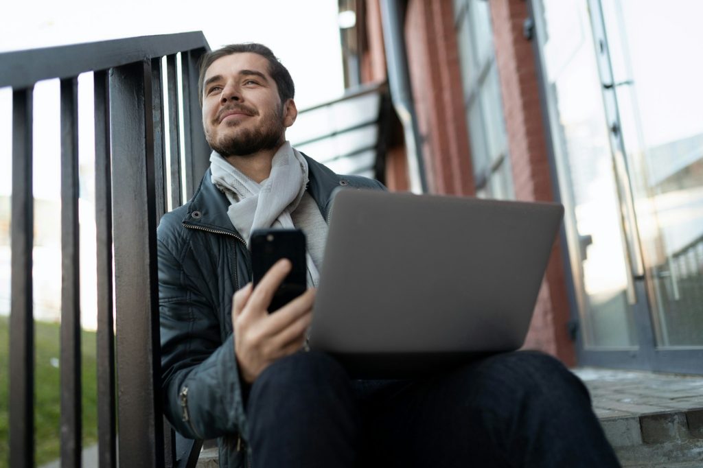 young man with laptop on his lap outside taking training courses